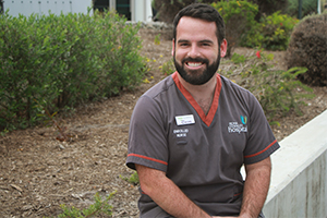 A man wearing nursing scrubs sits on a a garden wall