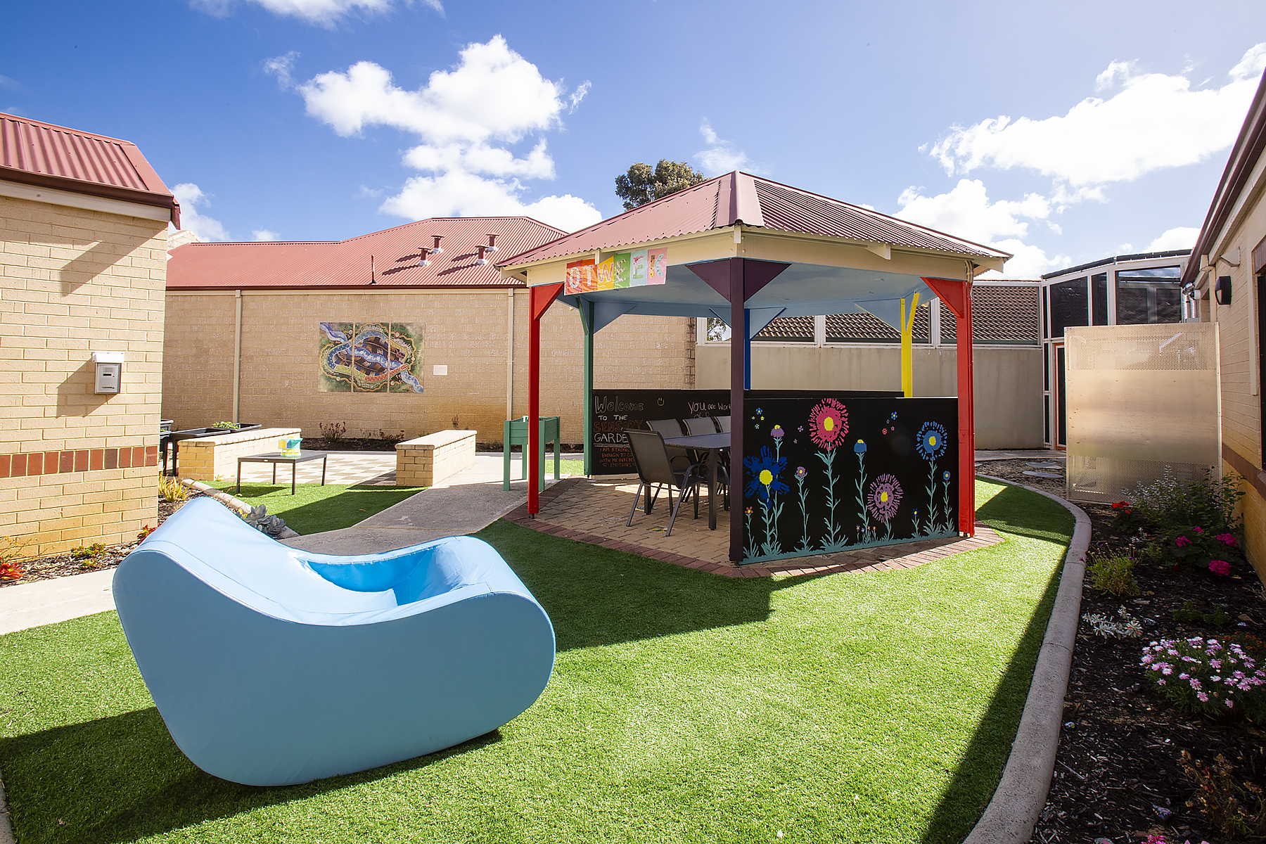 Picture of part of the new Therapy garden, with bright and colourful artwork, chairs and gazebo.